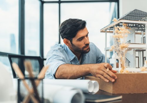 Portrait of smart caucasian engineer inspect house model. Closeup. Tracery. Closeup portrait of smart caucasian architect engineer inspect house model while thinking about building construction at architect studio on table with project plan, blueprint, equipment. Tracery.