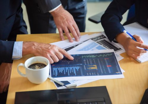 Unrecognizable businessman pointing at printed chart Unrecognizable businessman pointing at printed chart and showing graph to colleagues. Professional content partners making notes for statistics. Cooperation, communication and partnership concept